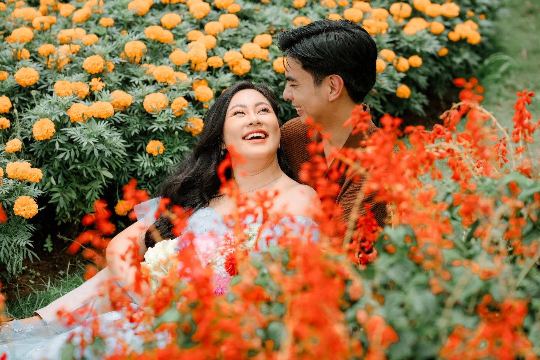 Luis and Tricia lying among marigolds and red salvia